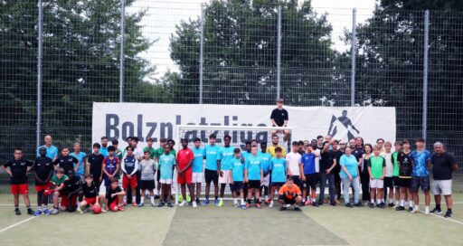 Gruppenbild mit Jugendlichen in Fußballkleidung und Erwachsenen vor einem Tor und einem Banner mit dem Schriftzug: Bolzplatzliga