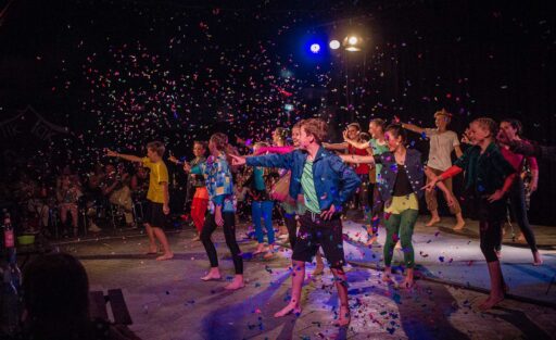 Kinder in Tanzbewegung bei einem Auftritt, von oben rieselt Konfetti