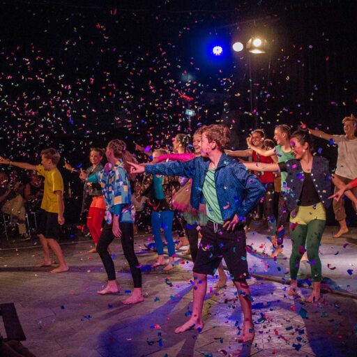 Kinder in Tanzbewegung bei einem Auftritt, von oben rieselt Konfetti