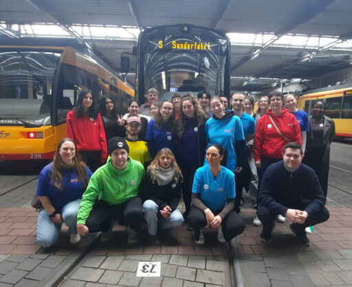 Das stja-Team im Straßenbahndepot vor einer Straßenbahn. Die digitale Anzeige der Bahn zeigt "Sonderfahrt"