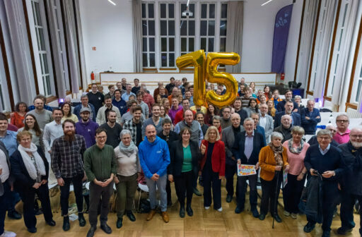 Blick von einer Bühne in das gesammelte, stehende Publikum. In der Mitte hält jemand die goldenen Zahlenluftballons für 75 Jahre. Im Hintergrund eine Fahne mit stja-Jubiläumslogo.