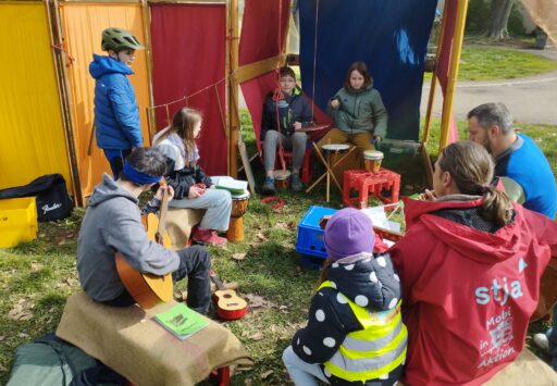 Kinder und Erwachsene sitzen im Kreis und musizieren.