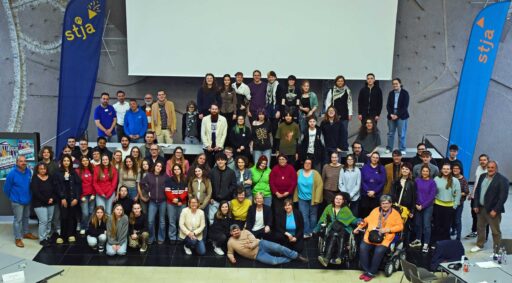 Gruppenfoto von Erwachsenen und Jugendlichen vor einer Leinwand und 2 stja-Flaggen