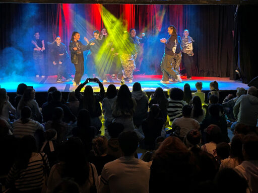 Blick auf eine Bühne mit Lightshow und tanzenden Jugendlichen, davor Publikum