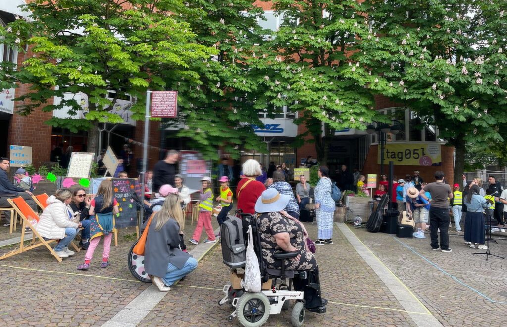 Buntes Treiben auf dem Kronenplatz mit Erwachsenen, Kindern, einer Frau im Rollstuhl.