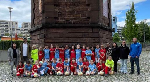 Gruppenbild der Mädchen- und Jungenmannschaft vor einem Wasserturm mit neuen Trikots. Bei den Mädchen in Rot, bei den Jungs in Blau.