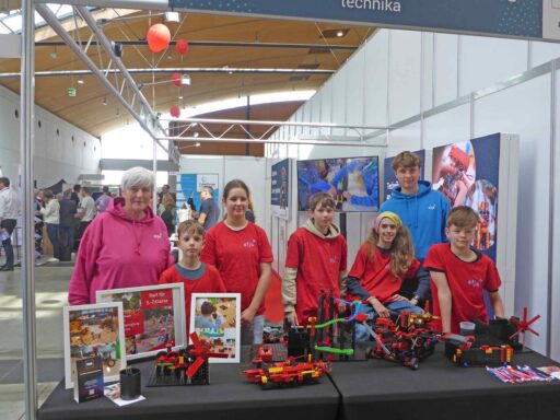 Fünf Jugendliche und zwei Erwachsene hinter einem Messestand. Davor ihre Bauwerke aus Lego.
