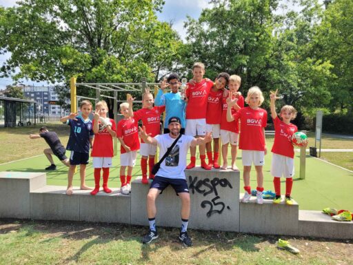 10 Fußballjungs in Trikots mit einem Pokal stehen auf Betonklötzen. In der Mitte sitzt Till Hofmann.