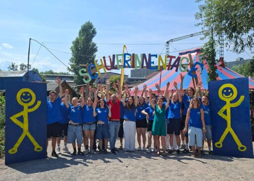 Jugendliche in blauen Shirts mit erhobenen Armen vor einem Schriftzug "Schülerinnentage". Dazwischen 2 Erwachsene.